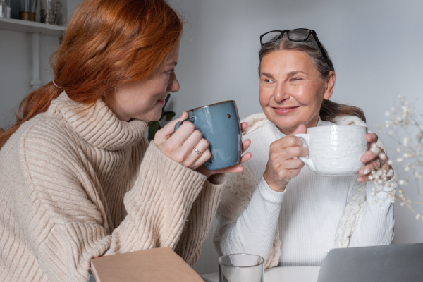 An adult child and an older parent talking warmly over coffee, representing a family money conversation.